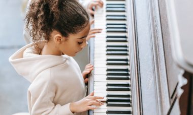 dziewczynka w bluzie z kapturem gra na fortepianie